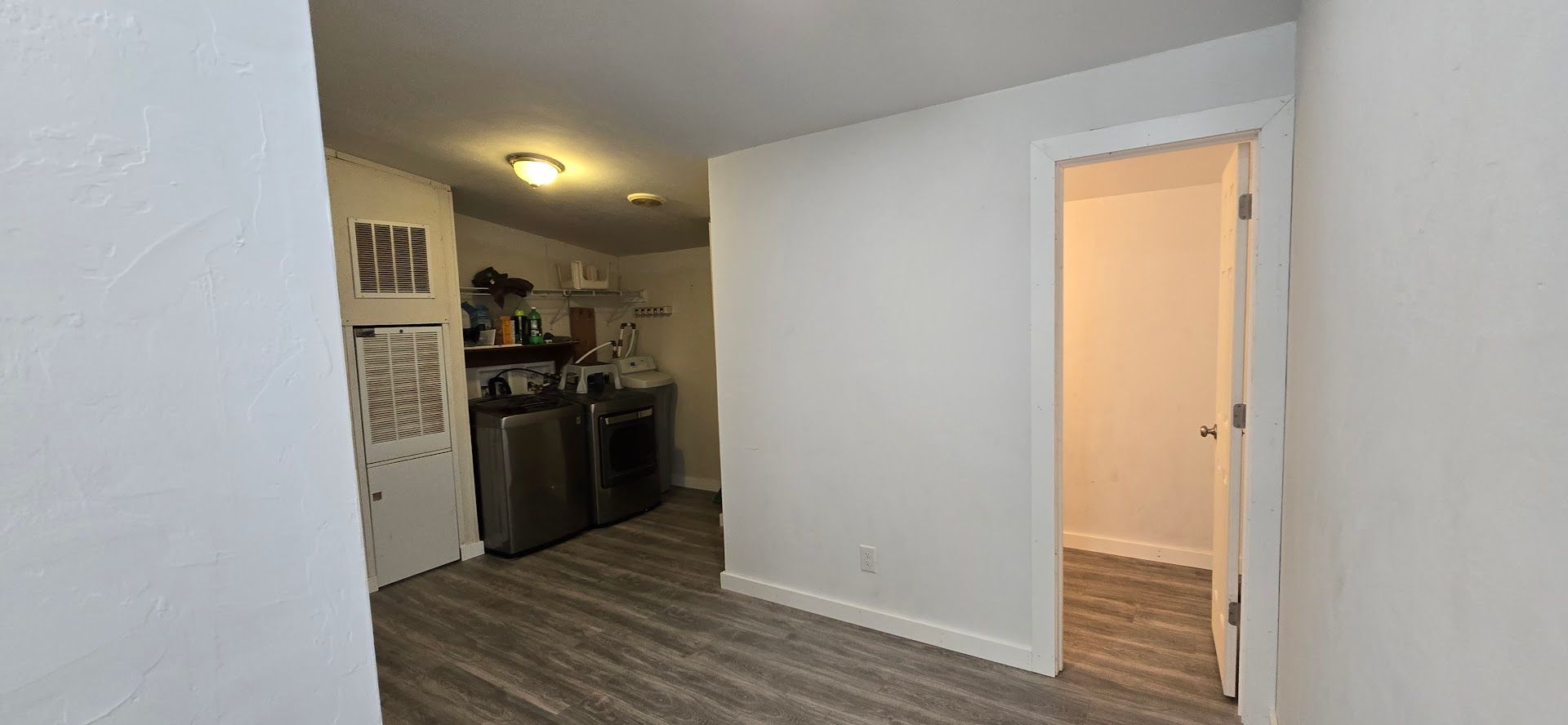 Empty apartment hallway leading to a small kitchen with dark cabinets and gray wood floors