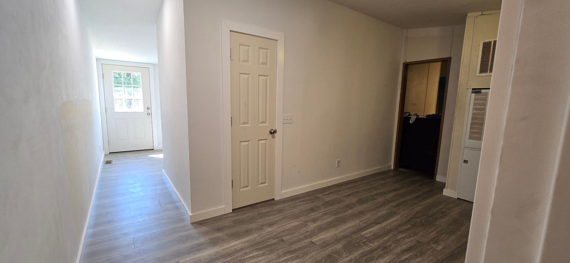 Empty hallway with white walls, gray carpet, and a bright doorway at the far end.