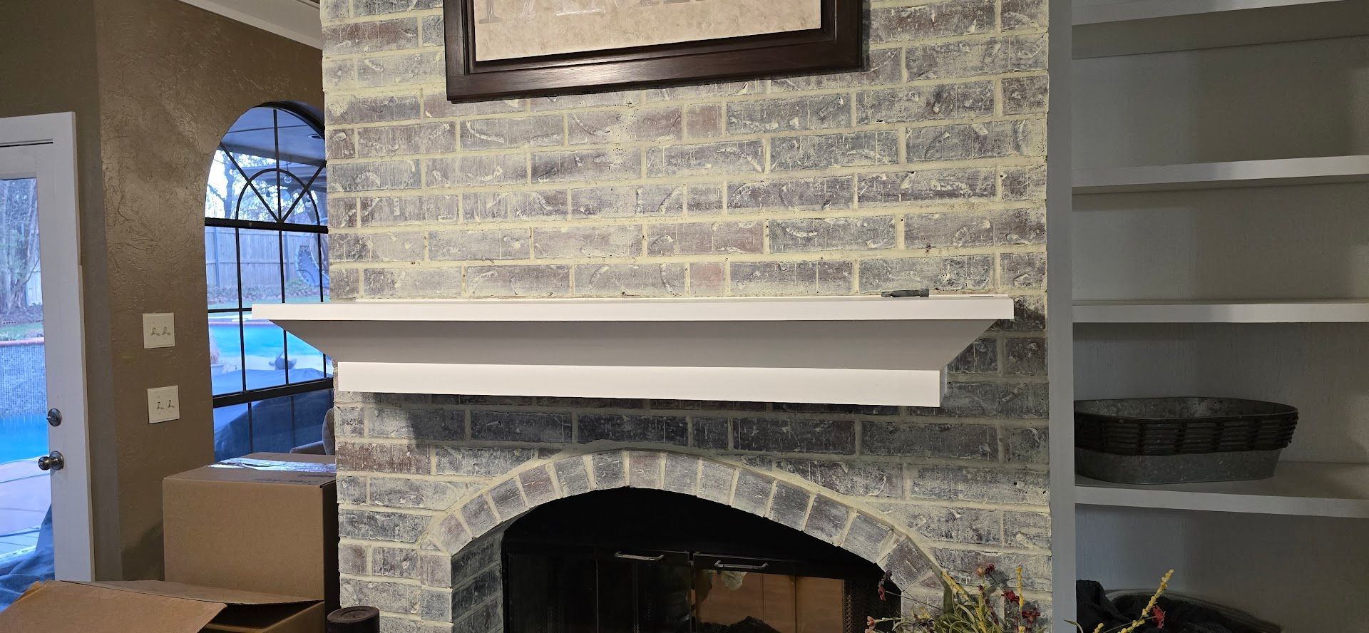 Built-in brick fireplace with white mantel in a living room, with shelves on the right and a window on the left