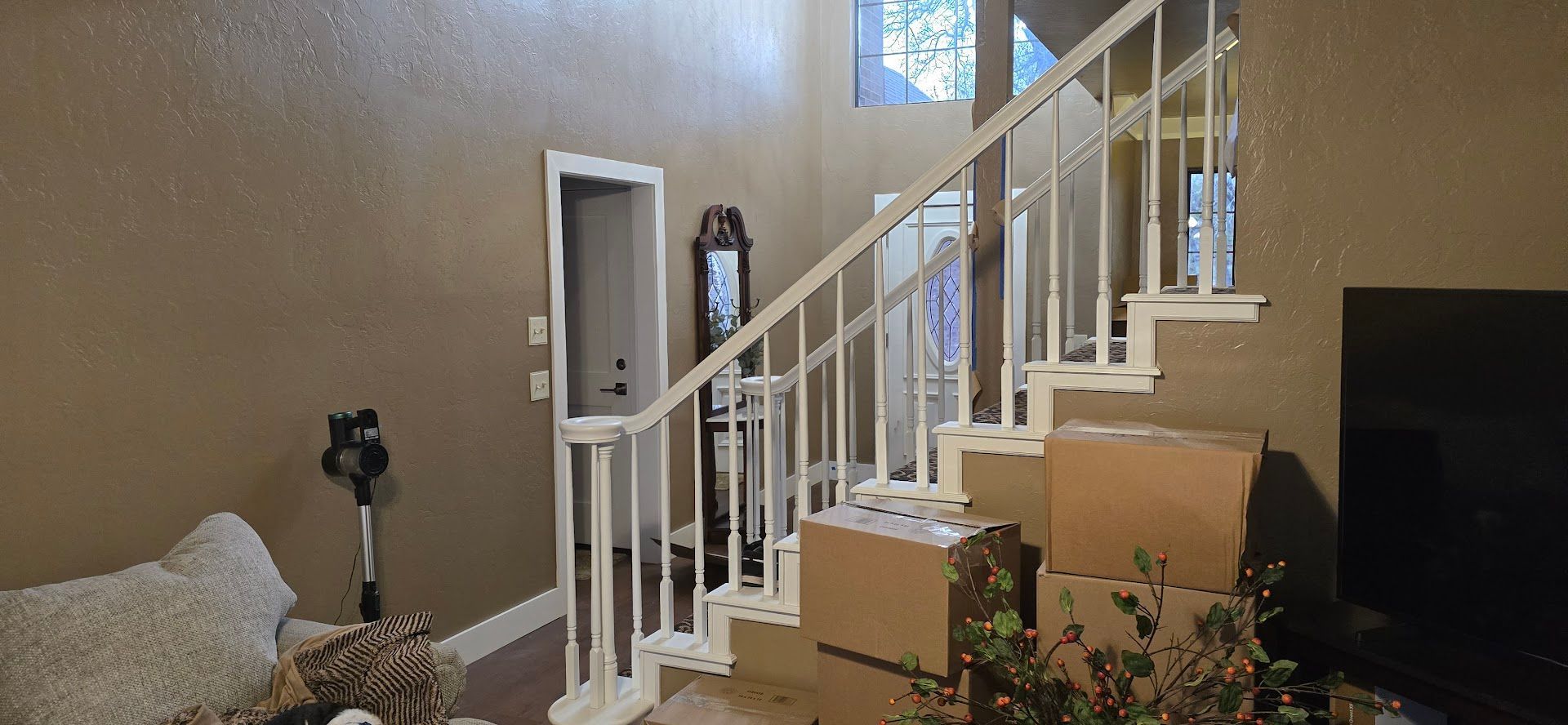 Living room staircase with white railing, beige walls, couch, plant, and TV
