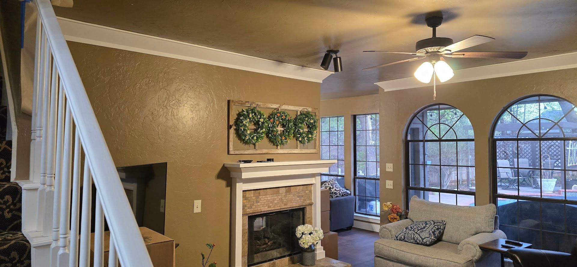 Living room with fireplace, white staircase, arched windows, and beige sofa under a ceiling fan