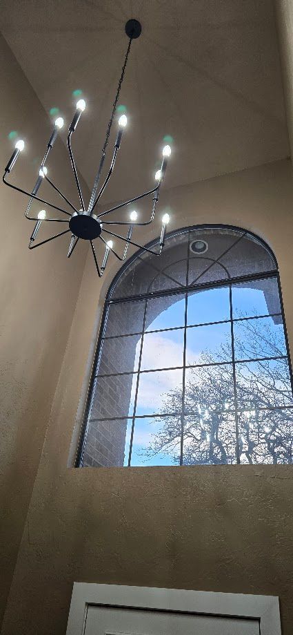Modern chandelier hanging beside an arched window with blue sky and tree visible outside