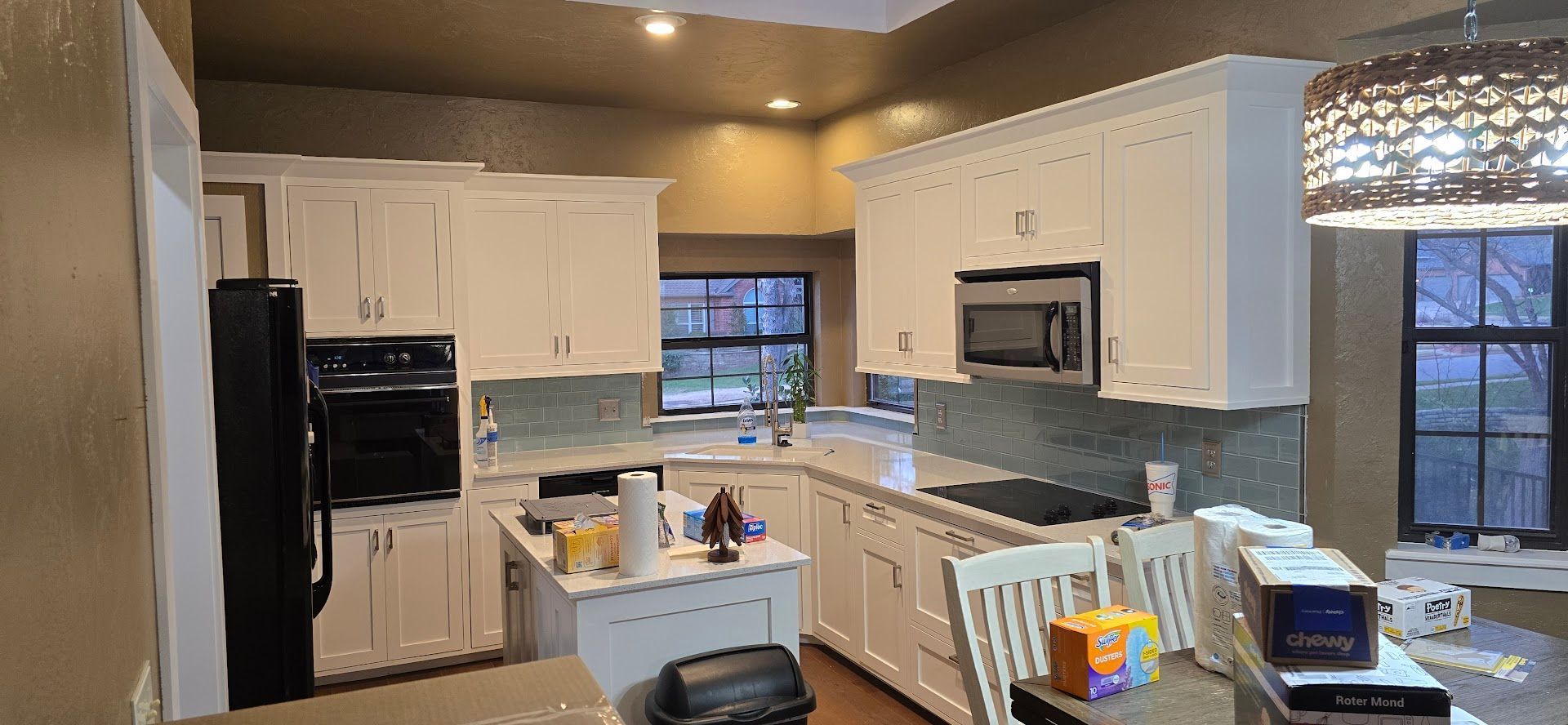 Modern kitchen with white cabinets, black appliances, gray tile backsplash, and a window over the sink