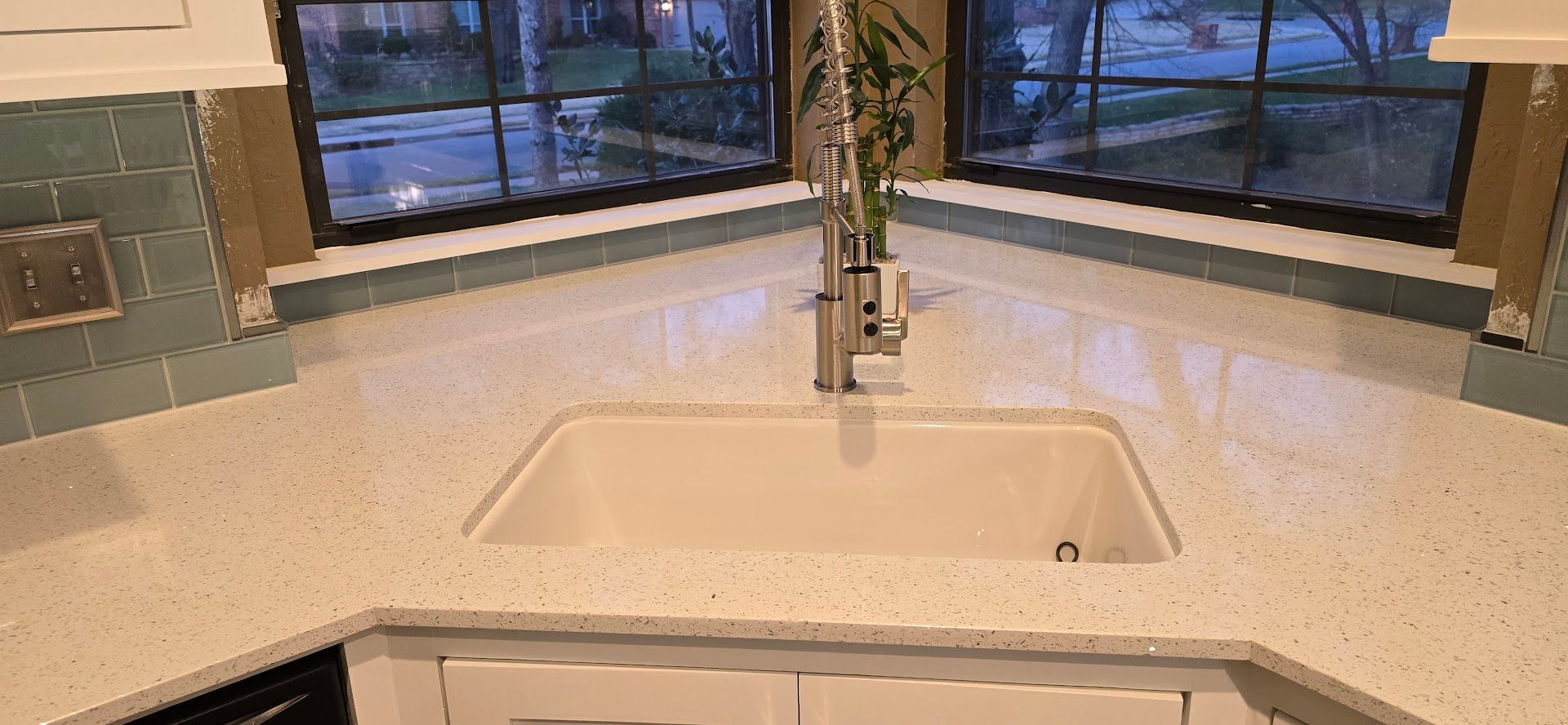 Modern kitchen sink with white countertop and large windows at dusk
