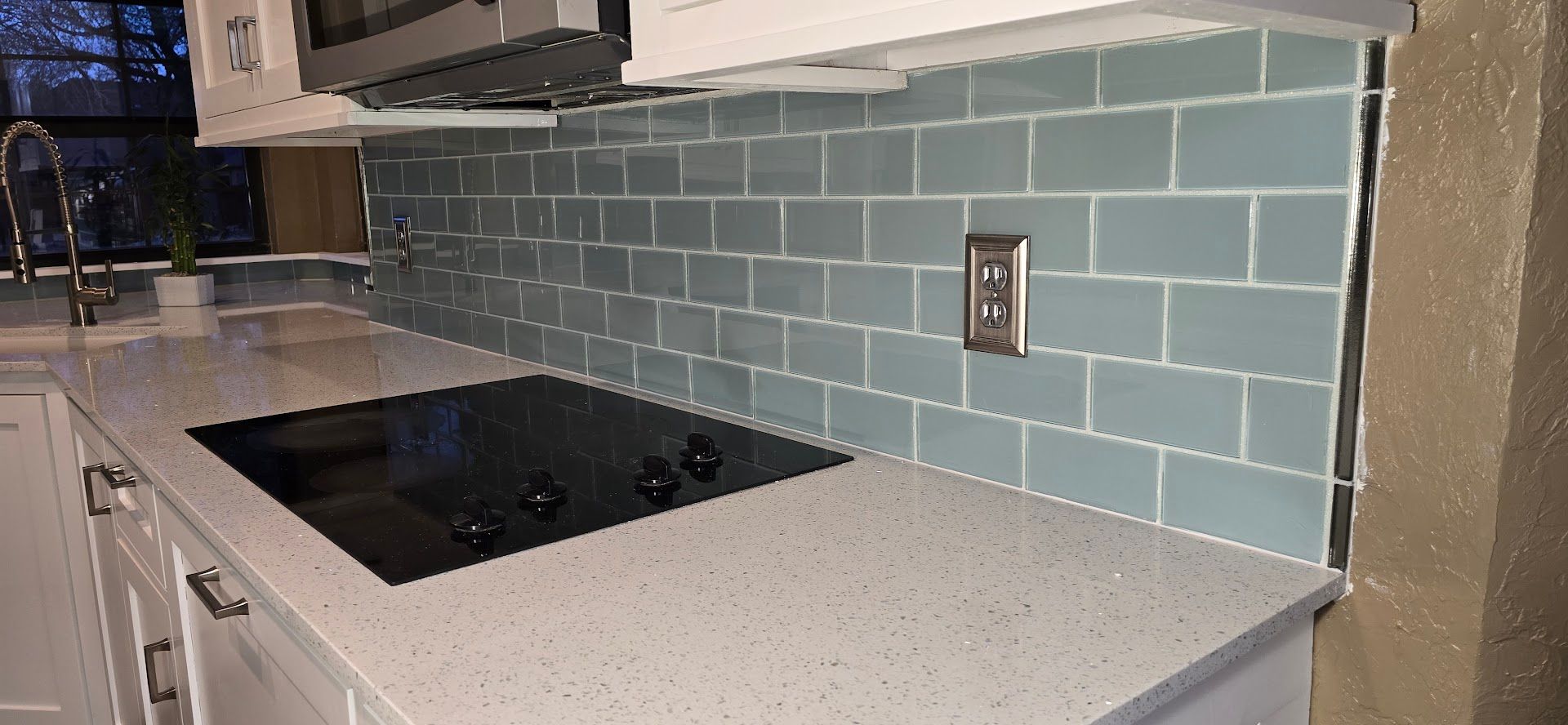 Modern kitchen countertop with black cooktop, gray subway tile backsplash, and light speckled counter
