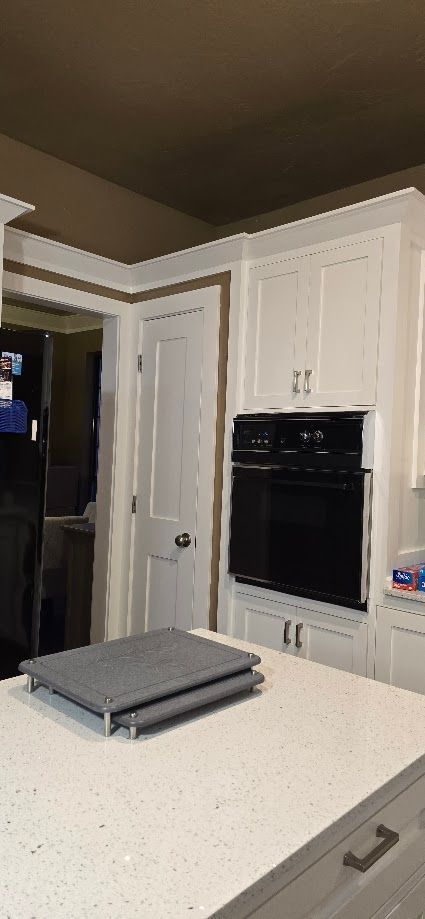 White kitchen with built-in black oven, cabinet doors, and a speckled countertop with folded towels.
