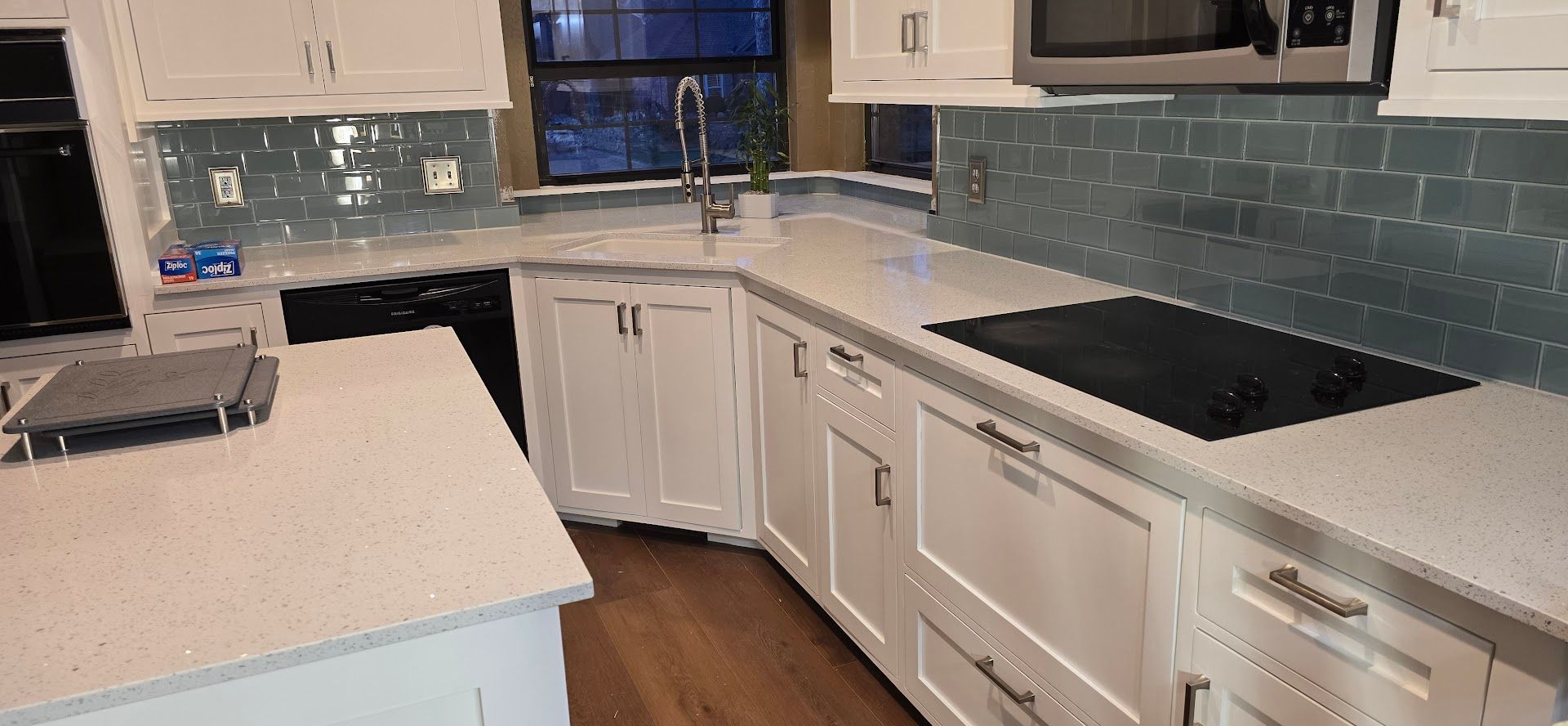 Modern white kitchen with island, black countertops, stainless appliances, and blue tile backsplash