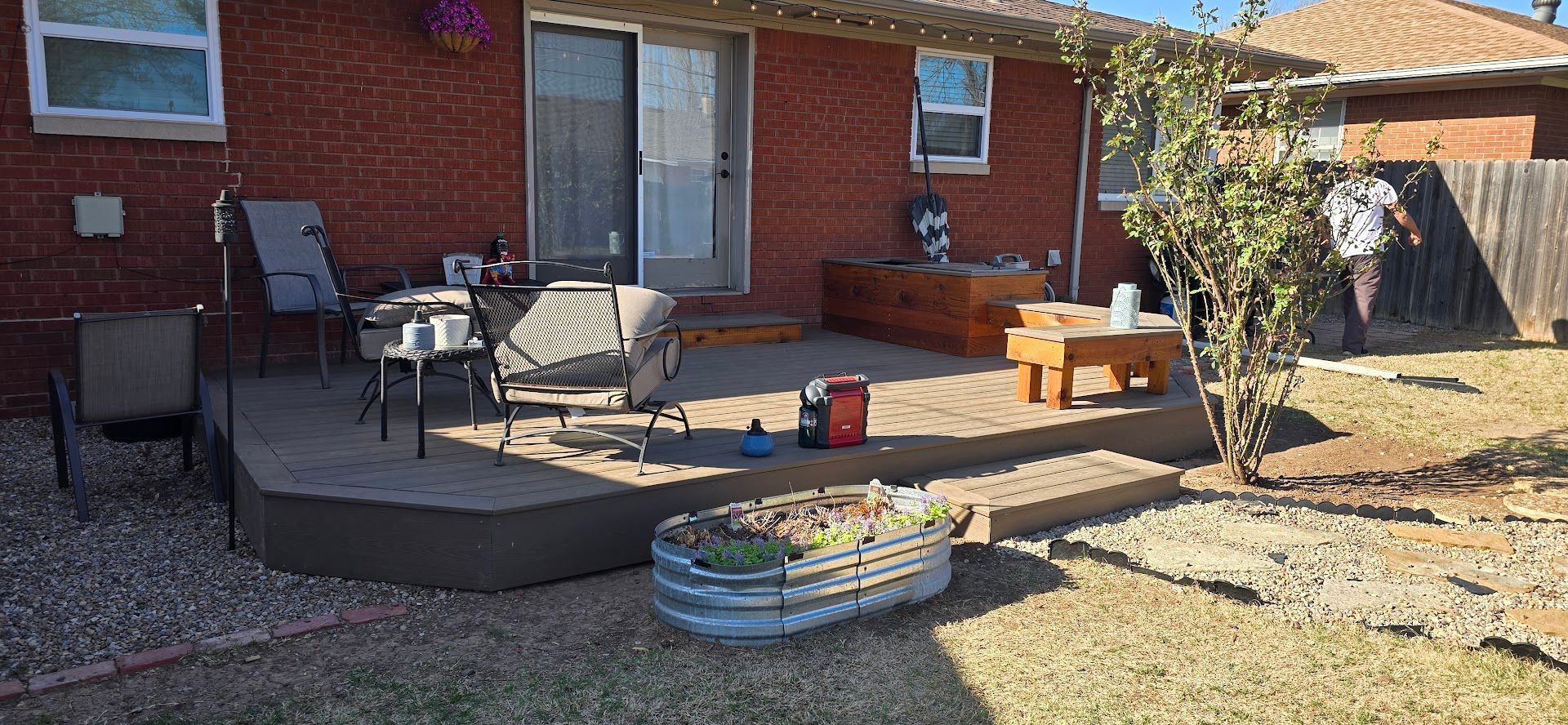 Backyard deck with patio furniture, fire pit, and raised garden bed beside a brick house