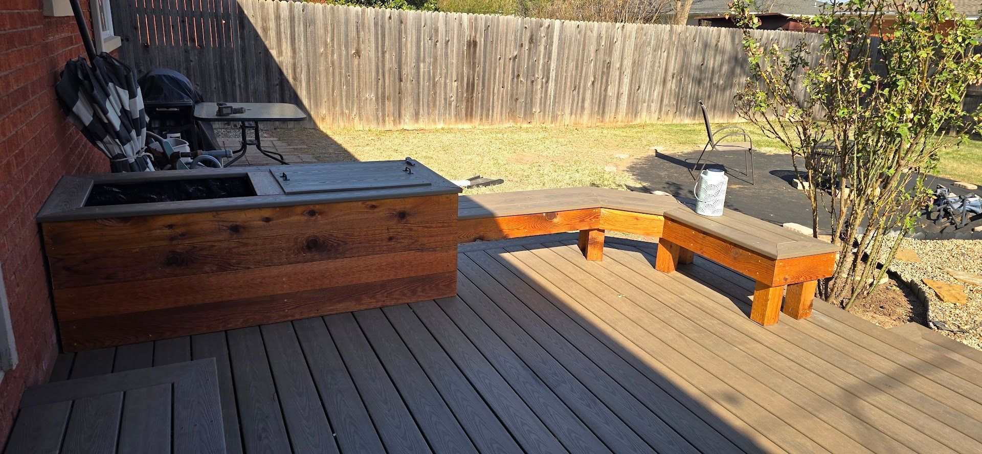 Outdoor wooden deck with built-in seating and a large wood hot tub or fire pit, near a fence and potted plants