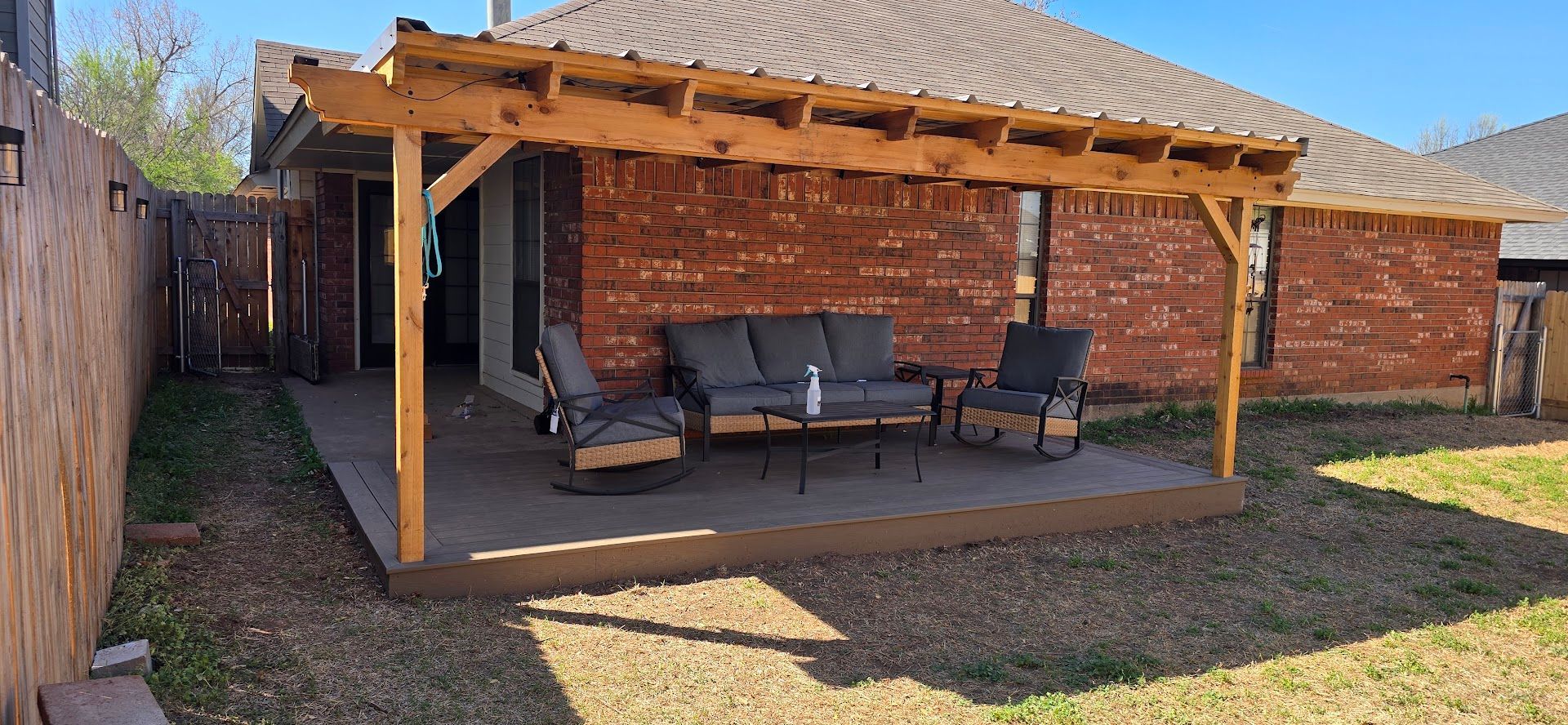 Covered brick patio with outdoor sofa and chairs in a sunlit backyard