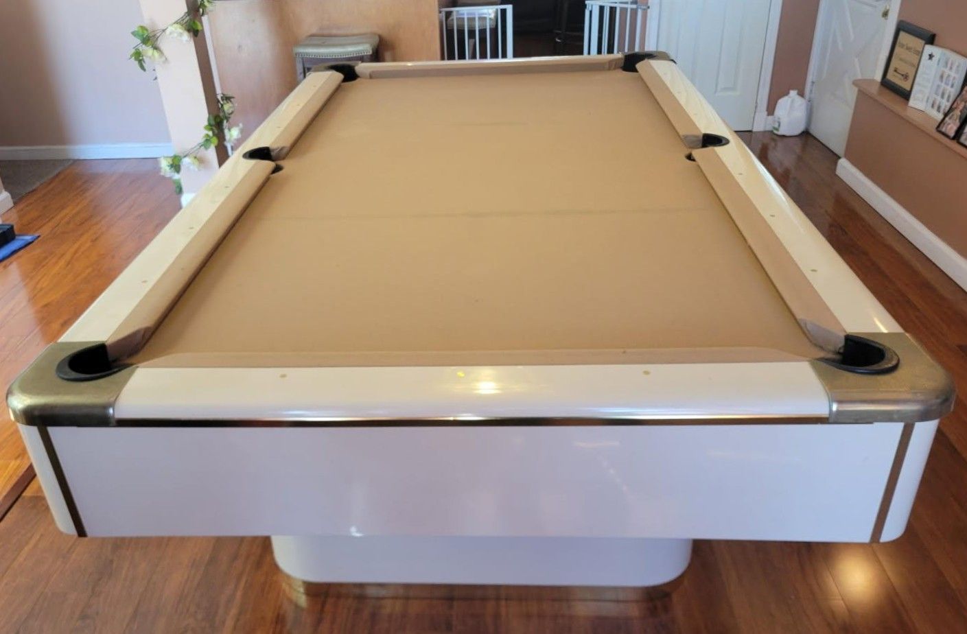 Tan pool table in a bright room, viewed from the end with white rails and black corner pockets
