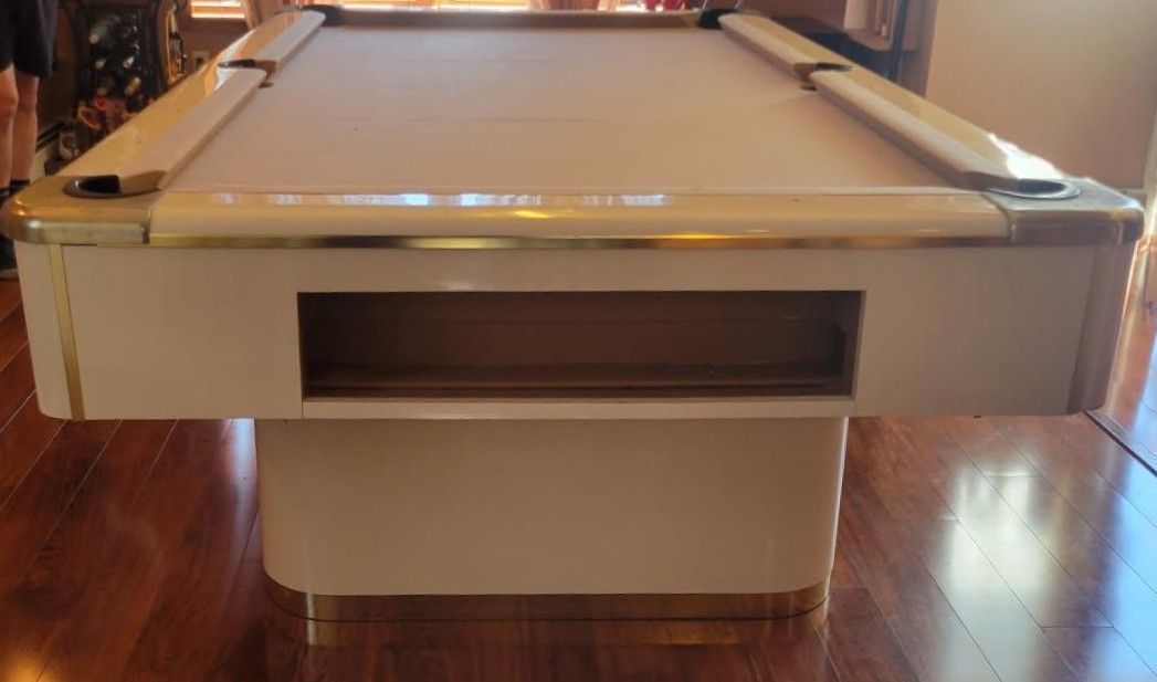 Front view of a white pool table with a beige cabinet base on a wooden floor.