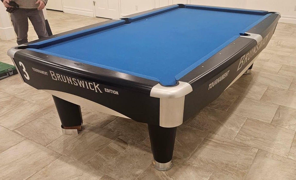 Blue-felt pool table in a tiled room, with a person standing beside it.