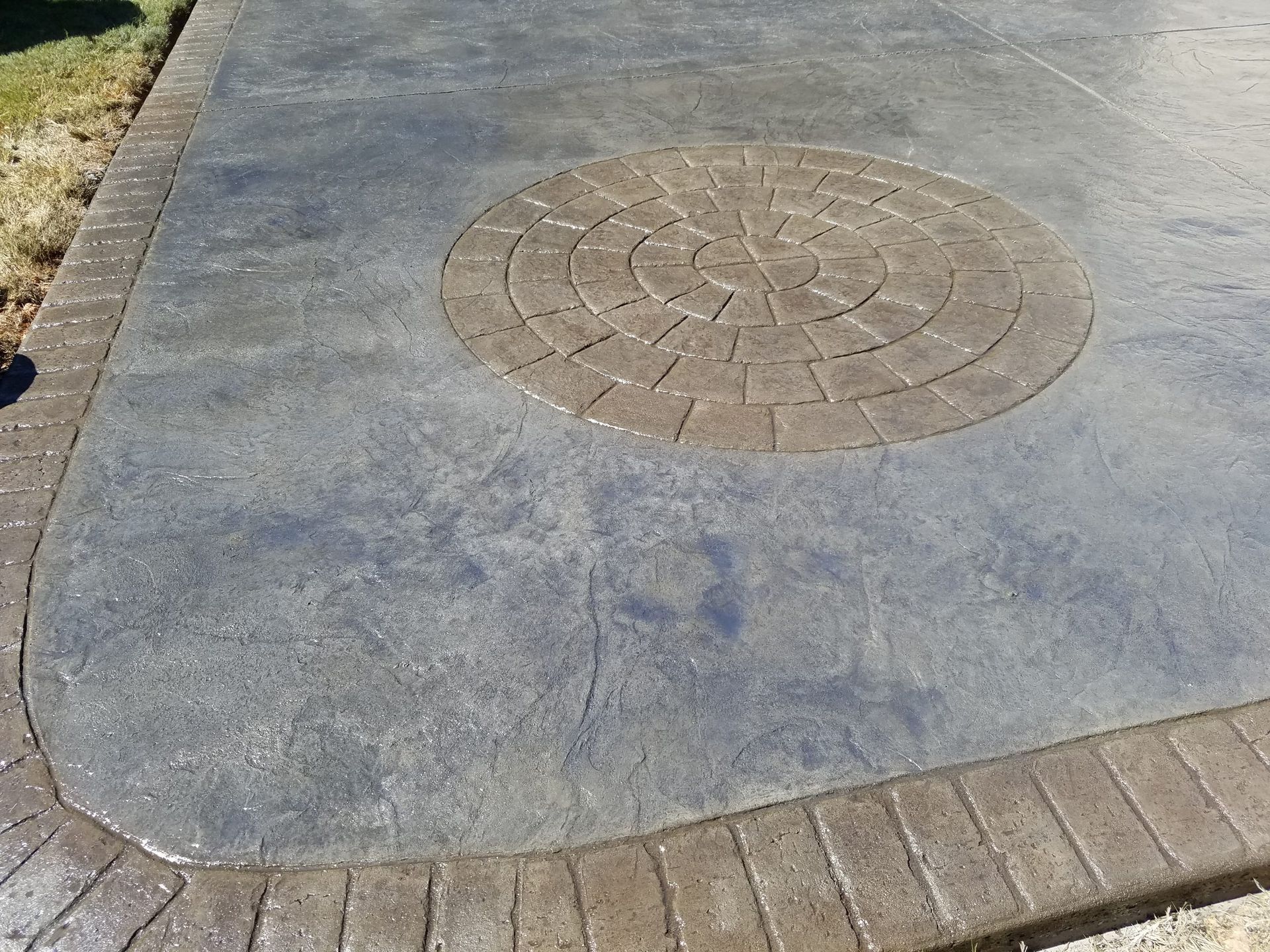 Concrete sidewalk with a round manhole cover and a brick border curve.