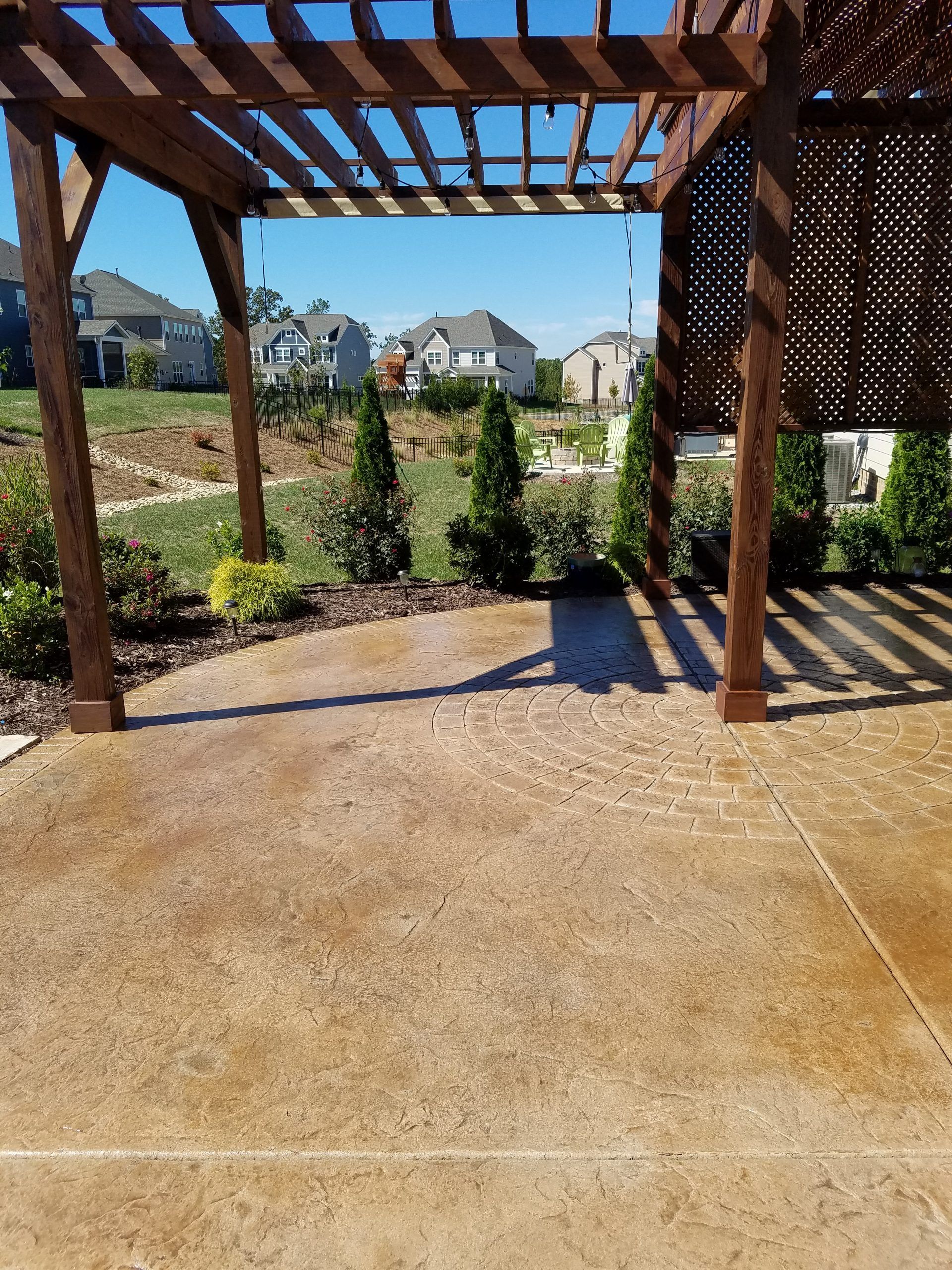Covered patio with wooden pergola, concrete floor, and landscaped backyard homes beyond.