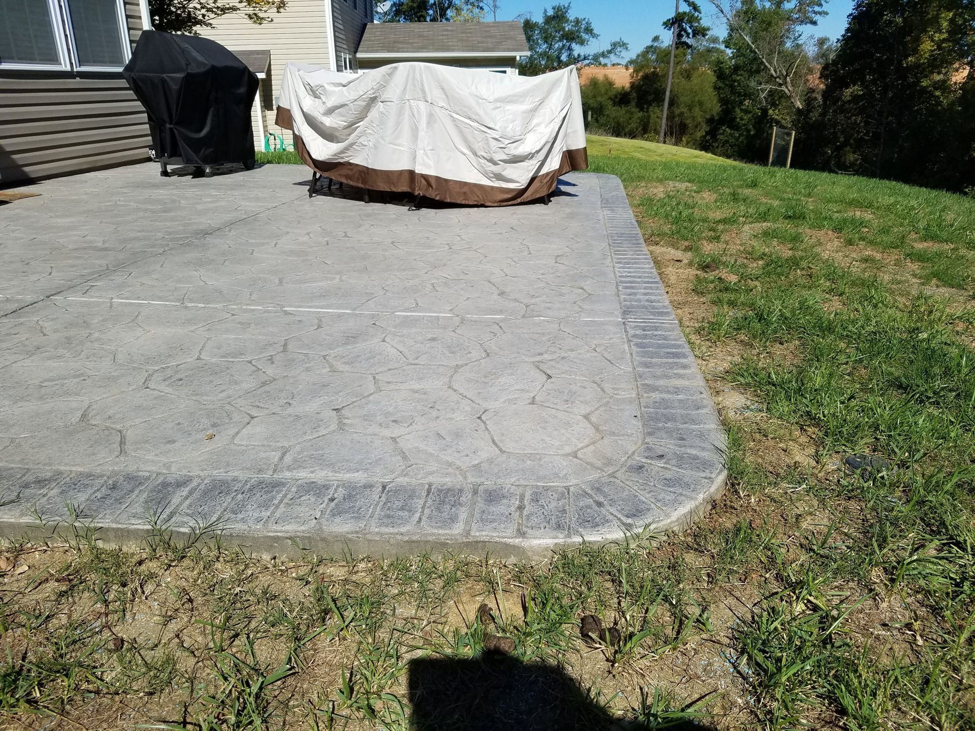 Covered patio furniture on a concrete patio beside a grassy yard in bright sunlight