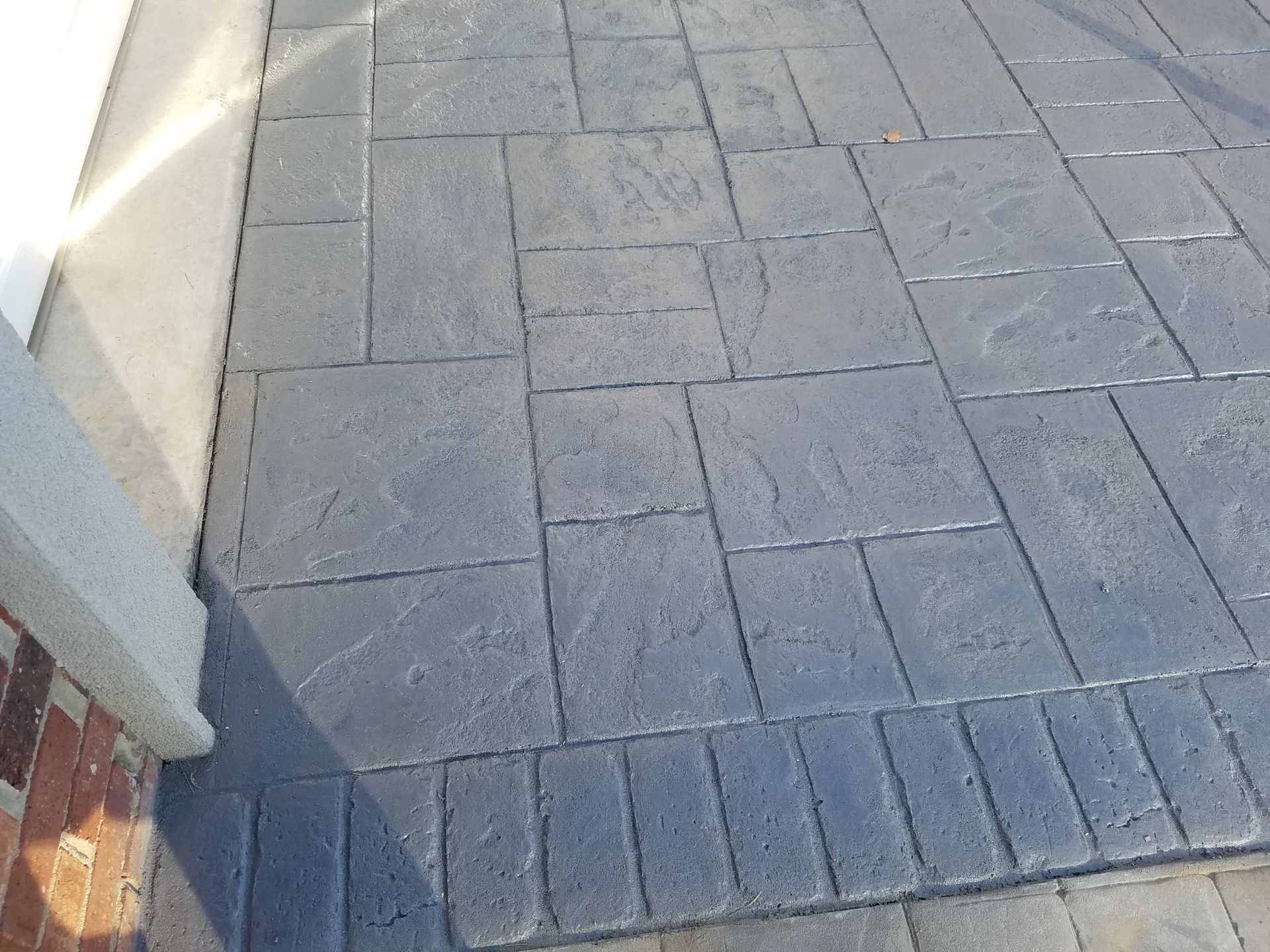 Paved sidewalk with gray brick pavers and a white wall edge in sunlight