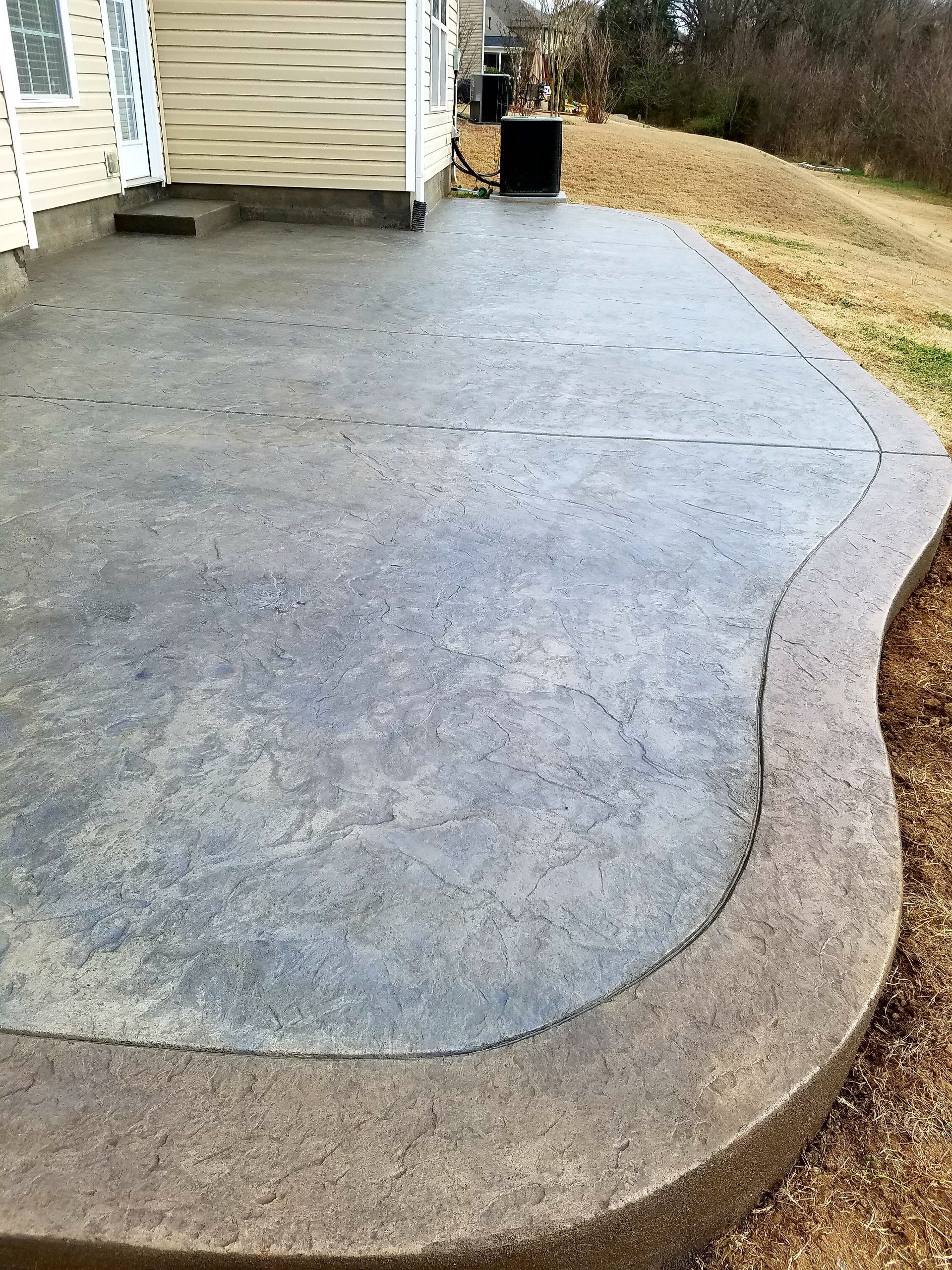 Freshly poured concrete driveway beside a house, with a curved border and gravel edge