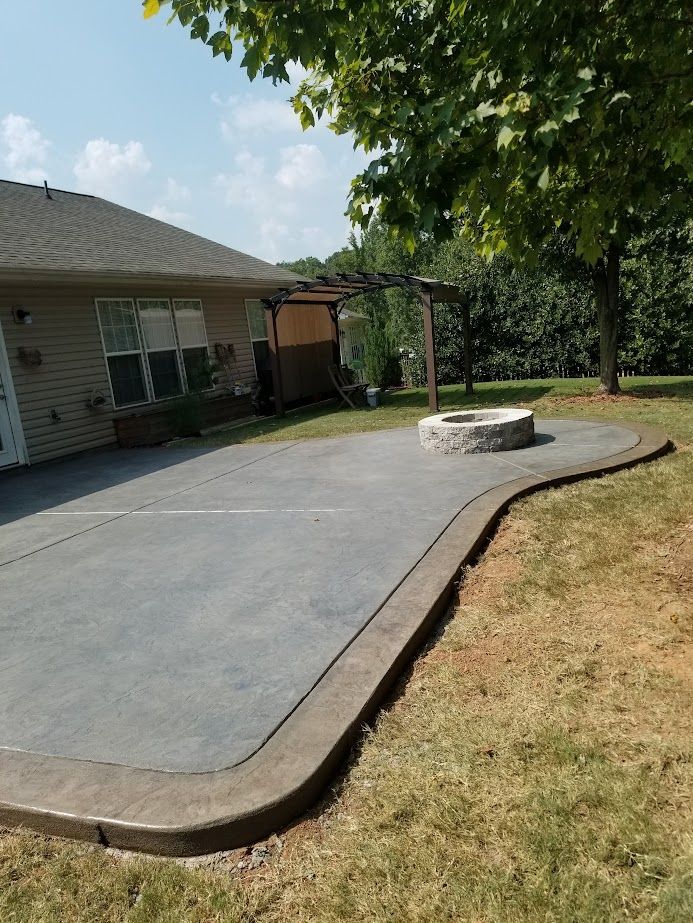 Backyard patio with smooth concrete, stone fire pit, and grassy yard beside a house
