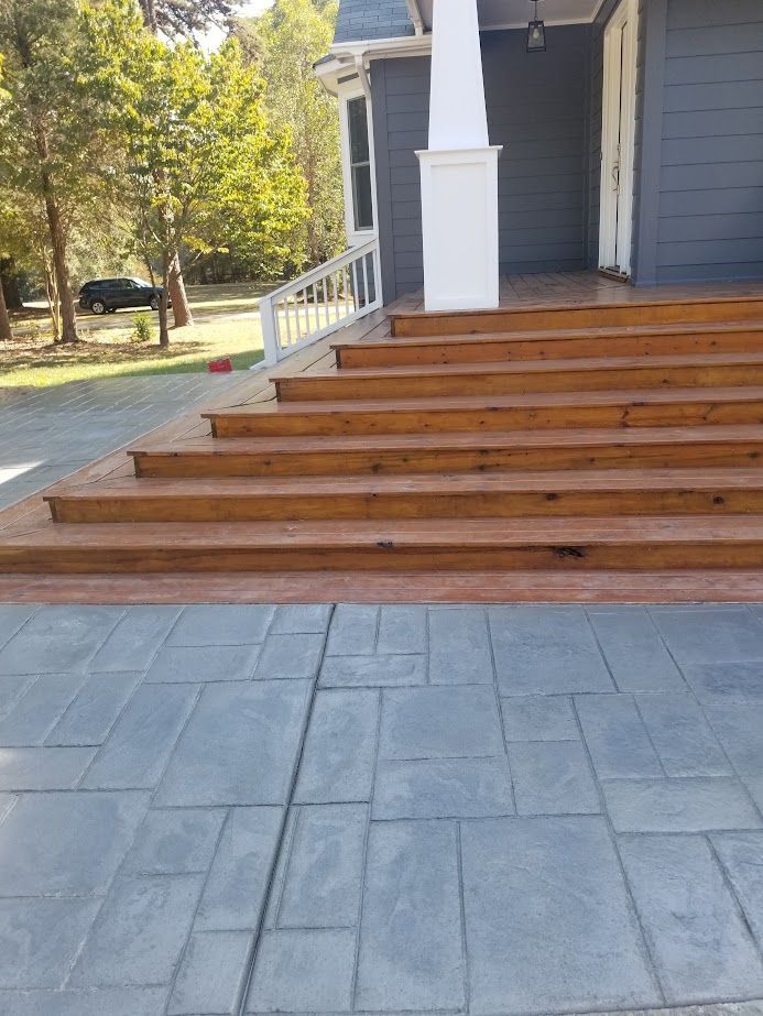 Front porch with wide wooden steps and gray stamped concrete walkway beside a blue house.