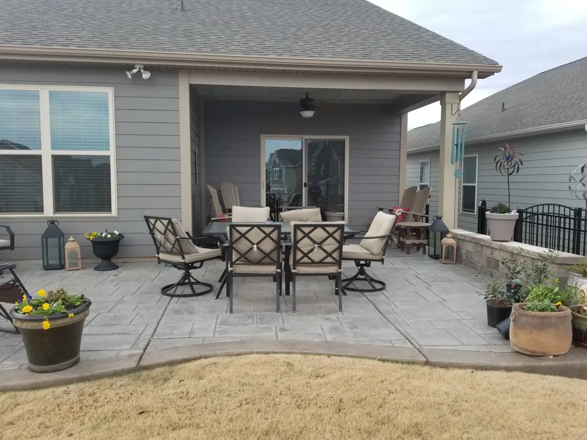Back patio with outdoor dining set, potted plants, and sliding glass door under a gray house overhang