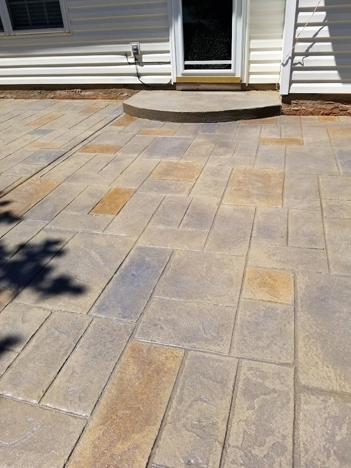 Stone patio walkway leading to a front door with a small curved step and white house siding