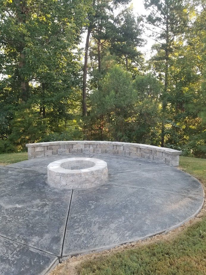 Circular stone patio with a central fire pit, surrounded by trees and a curved stone bench