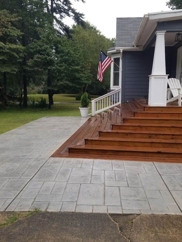 Front porch with brown steps, gray driveway, white railing, and an American flag beside a gray house.