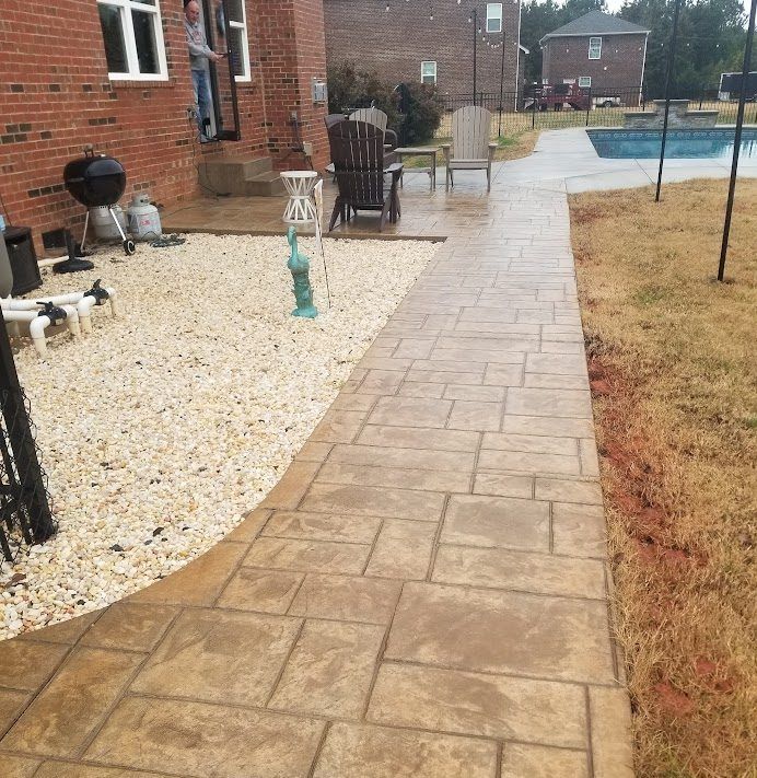 Rainy backyard patio with a stone walkway beside a brick house and pool.