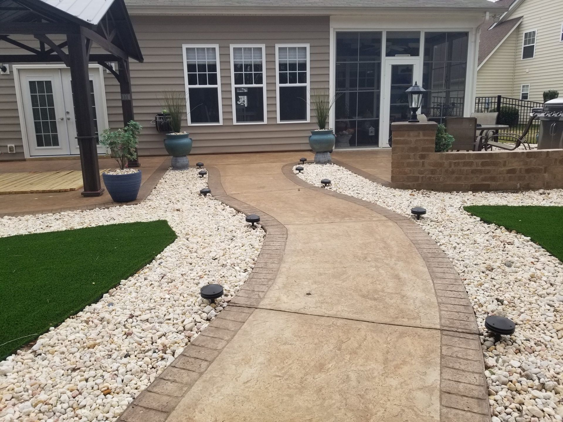 Curved concrete walkway leading to a front porch, bordered by white rocks and green lawn.