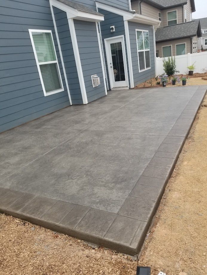 Concrete front patio beside blue house with white trim and gravel yard.