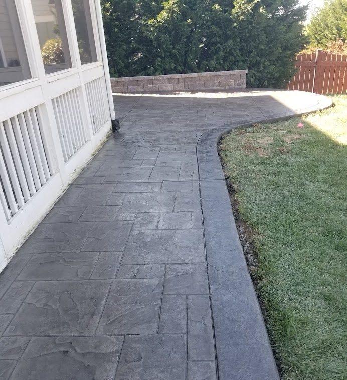 Stamped concrete patio beside a house, curving toward a stone wall and grassy yard.