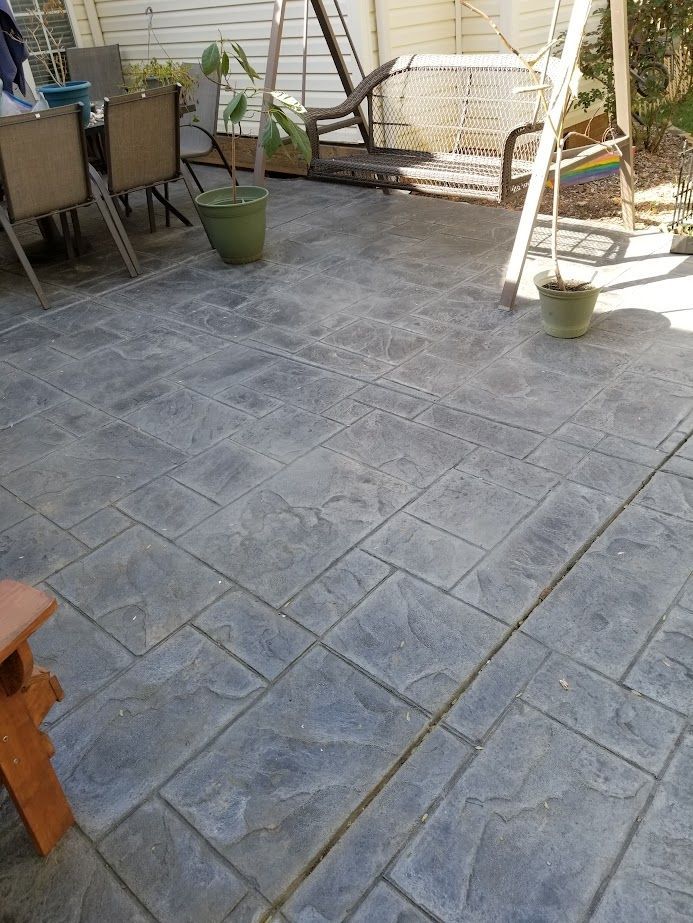 Stone patio with square pavers, potted plants, and outdoor furniture beside a house wall