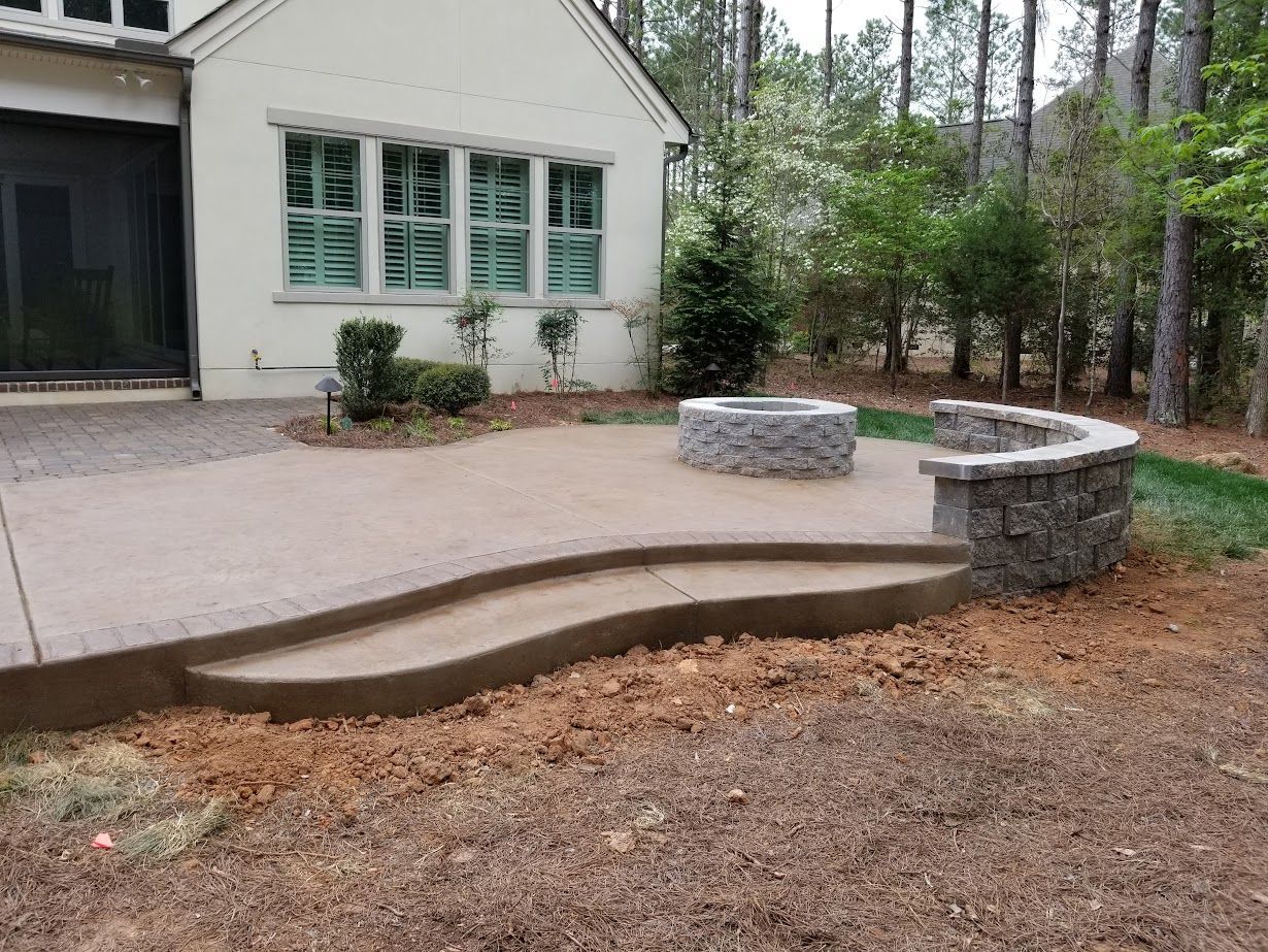 Stone patio with curved steps and built-in seating beside a house and wooded yard