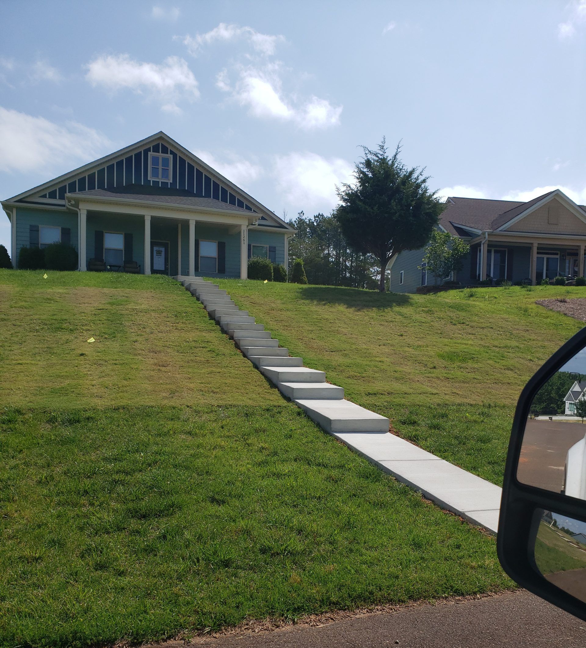 House with a steep concrete walkway up a grassy hill under a blue sky