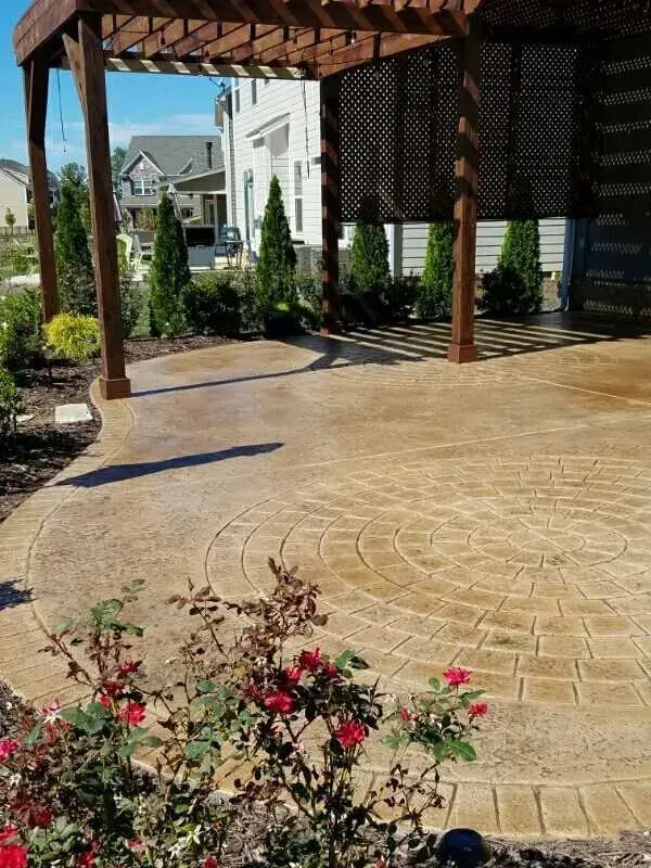 Covered brick patio with pergola, circular stone pattern, and flowering shrubs in a landscaped courtyard.