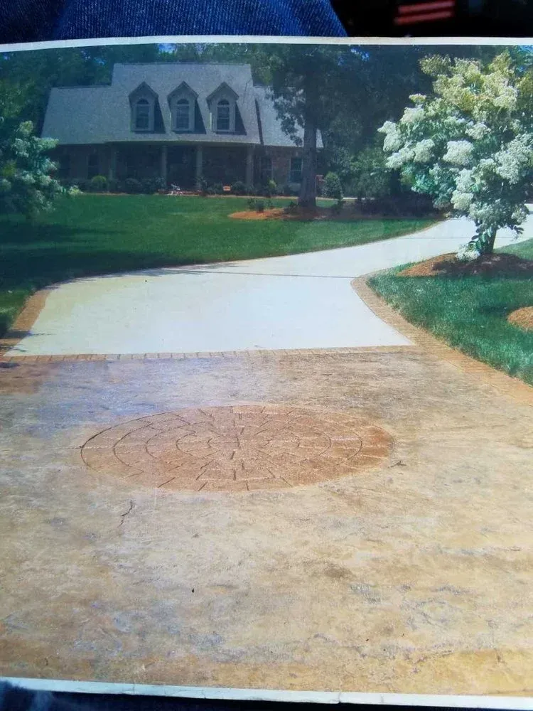 Driveway with a large circular stain leading to a suburban house with a green lawn and white flowering tree.