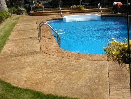 Curved concrete pool deck beside a blue swimming pool with a person near the far edge