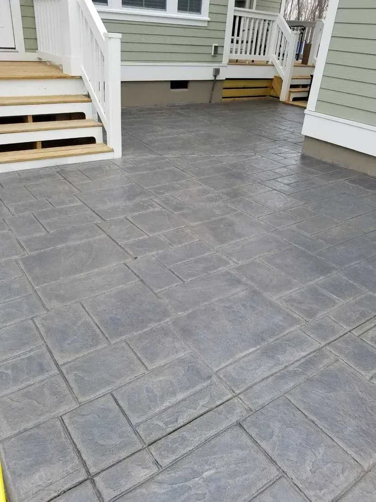 Gray paver patio between two houses with short steps and beige siding