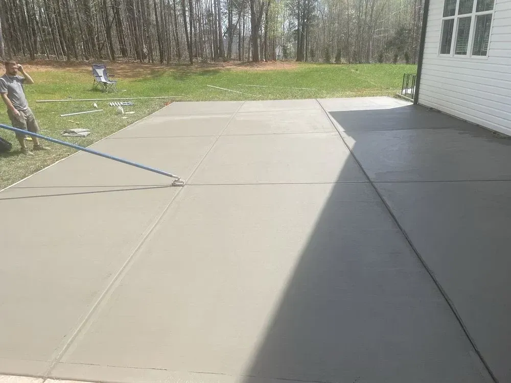 Workers smoothing a fresh concrete patio beside a white house on a sunny day