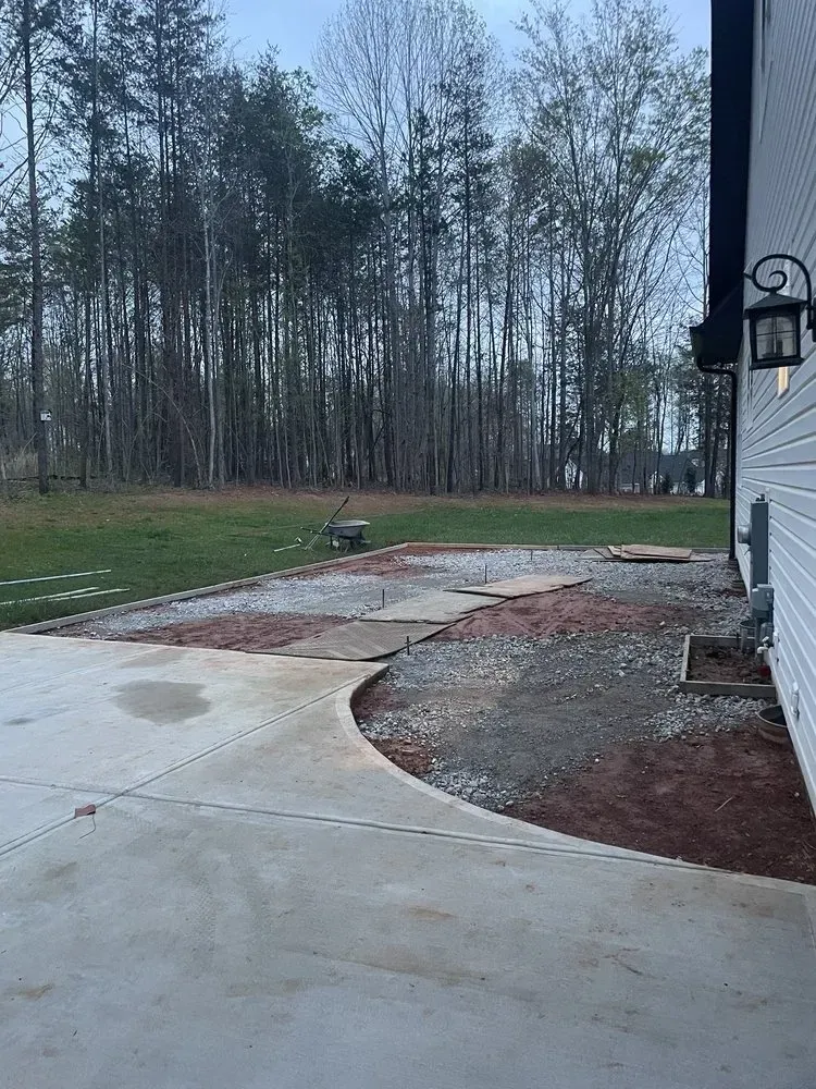 Wet concrete patio beside a house, with a muddy yard and leafless trees in the background.