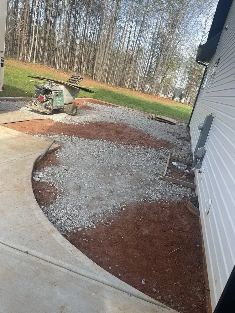 Gravel and red mulch landscaping beside a white house, with a lawn tractor in the background.