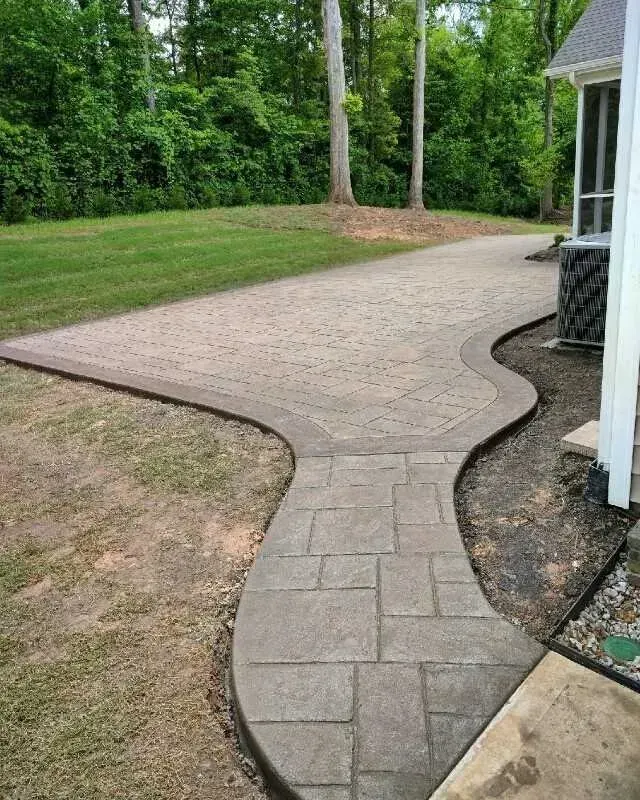 Curved stamped-concrete walkway leading through a green yard beside a house porch