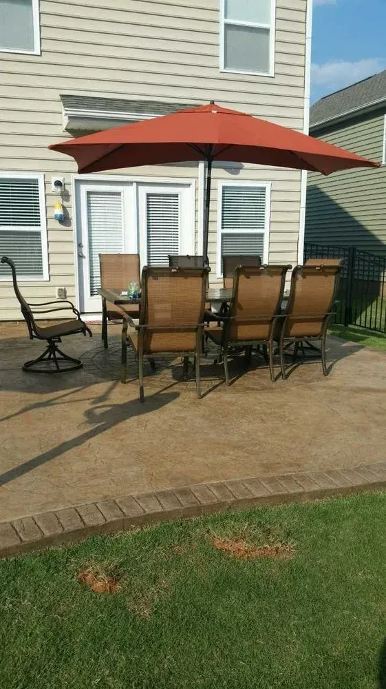 Patio table and chairs with red umbrella on a backyard deck beside a house