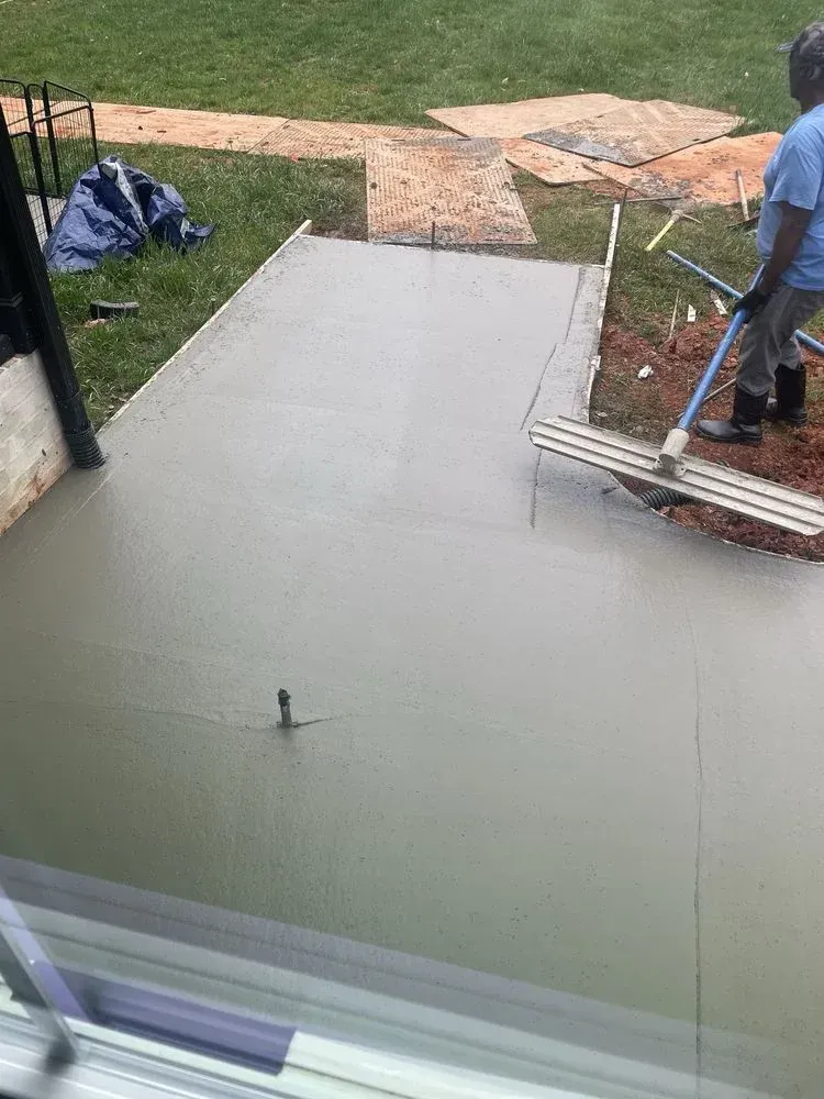 Freshly poured gray concrete patio beside a grassy yard, with a worker at the edge.