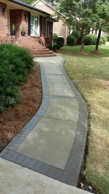 Curved concrete walkway with gray brick edging leading to a brick house and landscaped yard