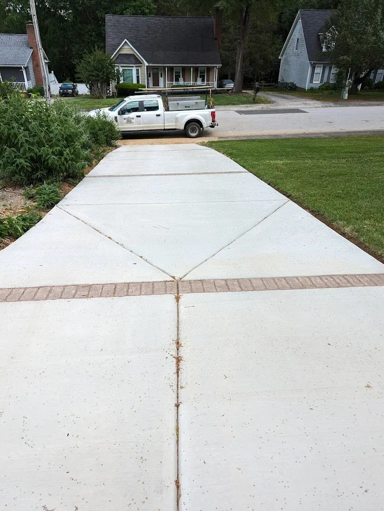 Concrete driveway leading to a street with a white pickup truck and houses in the background