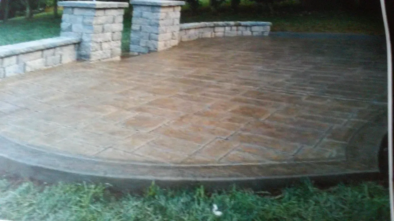 Stone patio with curved edge and stone railing posts beside grass.