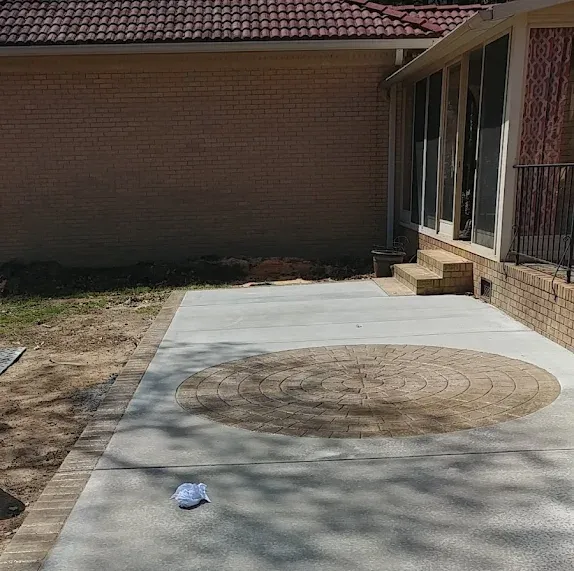 Concrete patio beside a brick house, with a circular stained area and a small white object on the ground.