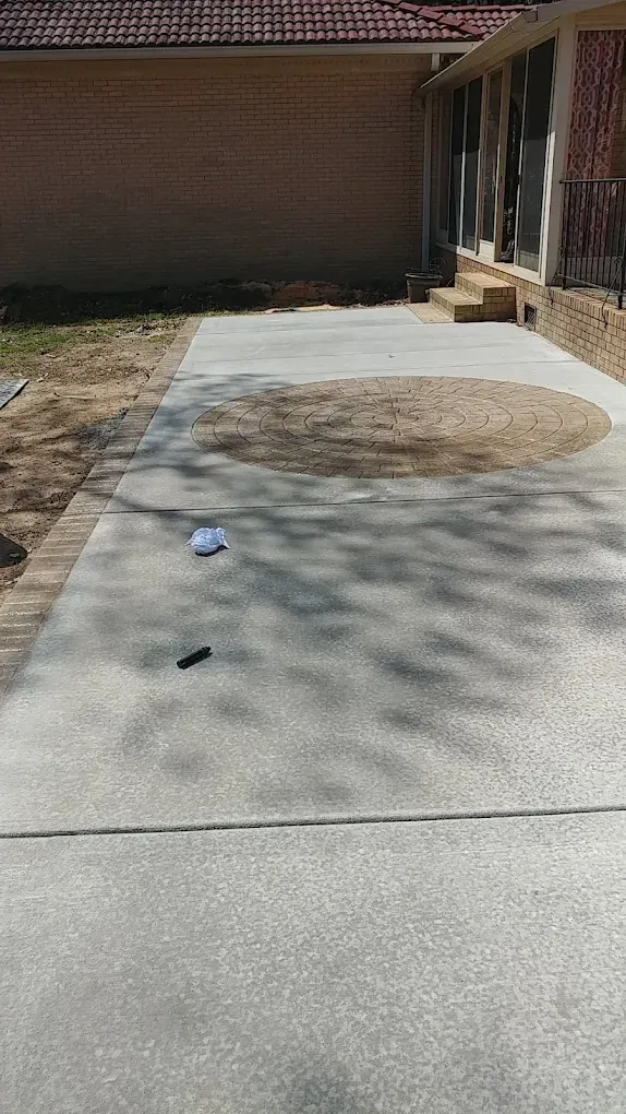 Concrete patio with a large white patch, a small object on the ground, and a brick building in the background